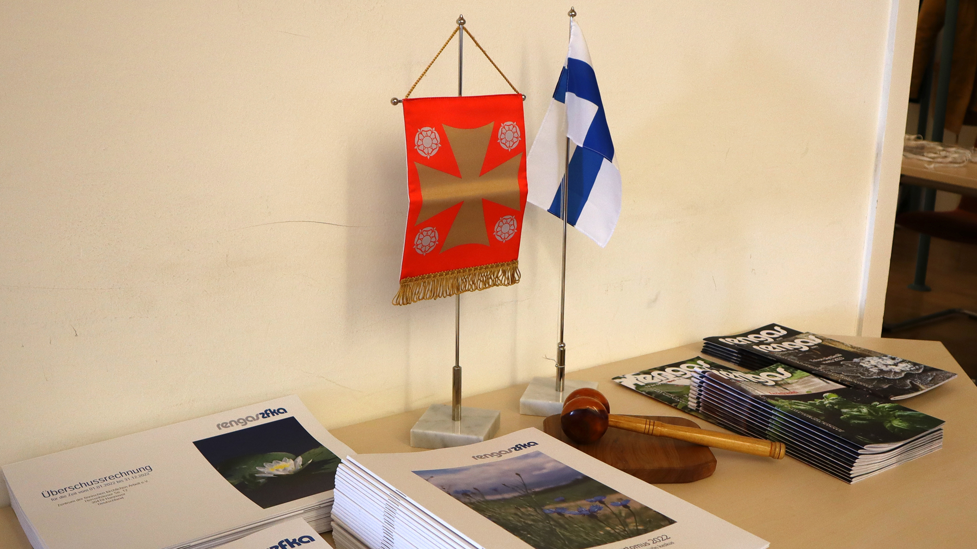 Suomen ja kirkon liput, puheenjohtajan nuija ja lehtiä pöydällä