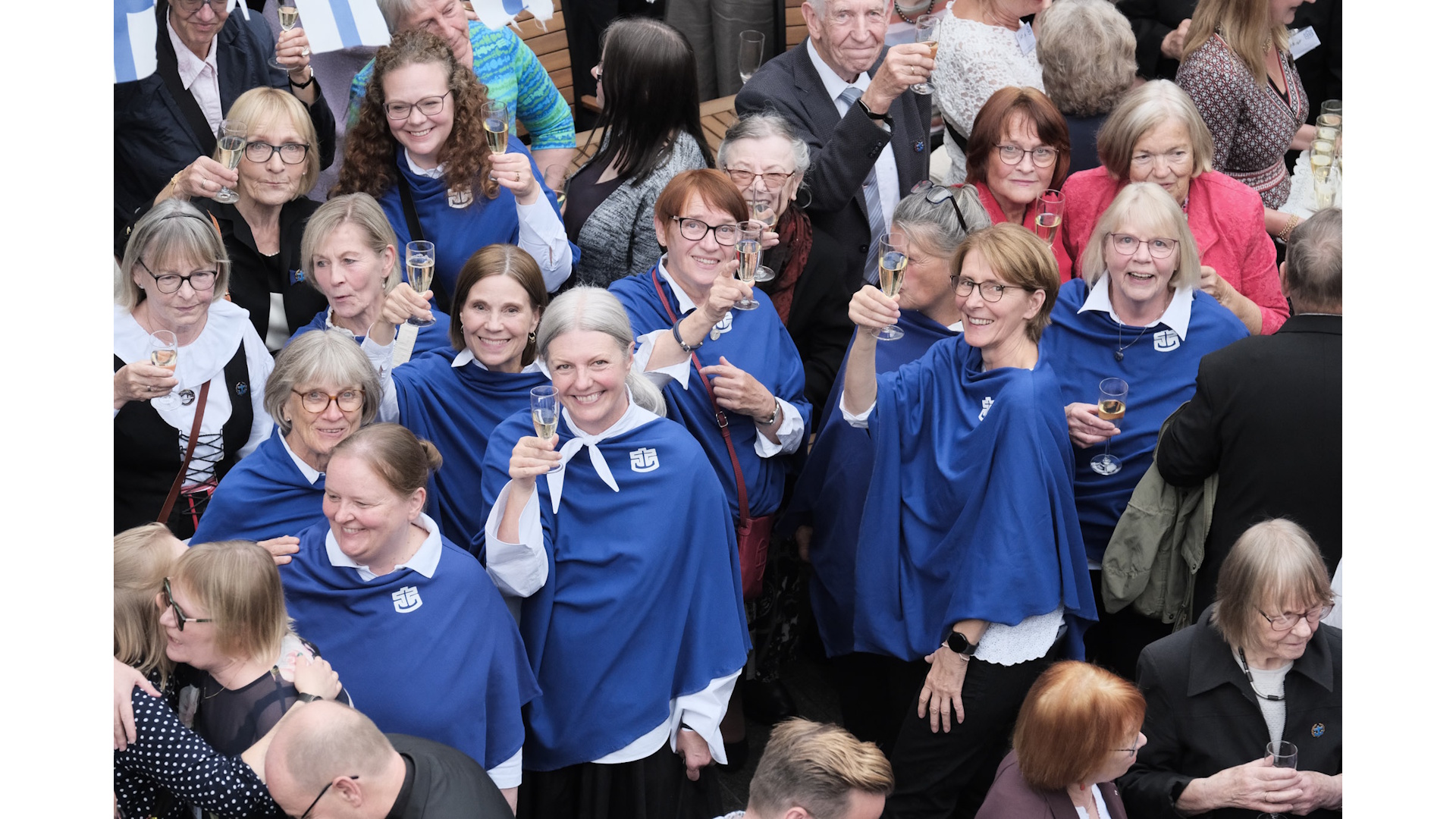 merimieskirkon kuorolaiset kohottavat maljan sinisissä viitoissa, joissa kirkon logo