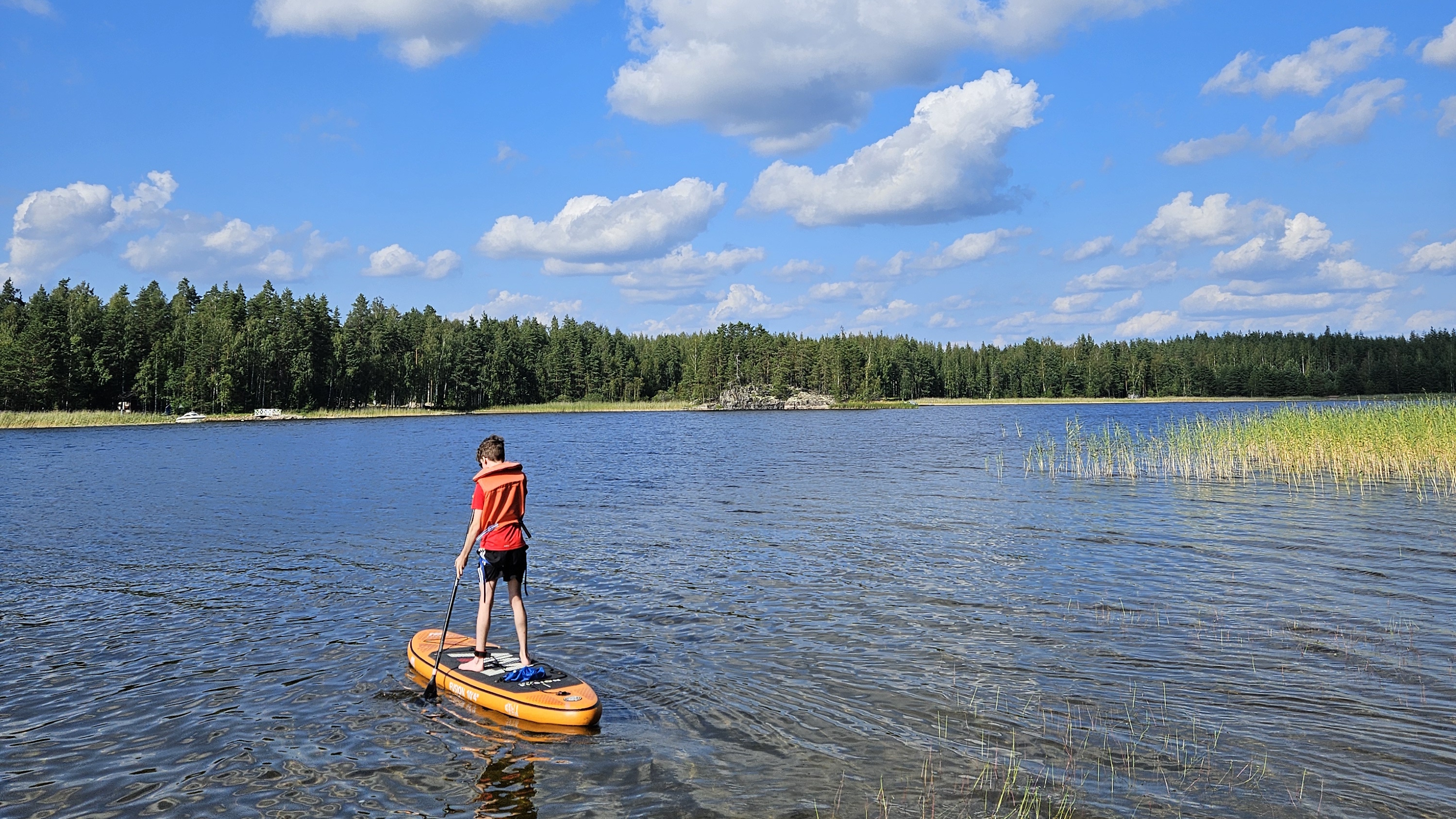 lapsi sup-laudalla kesäisessä järvimaisemassa