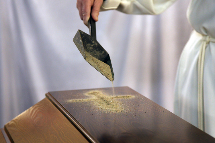 Pappi piirtää hiekalla ristinmerkin arkulle.