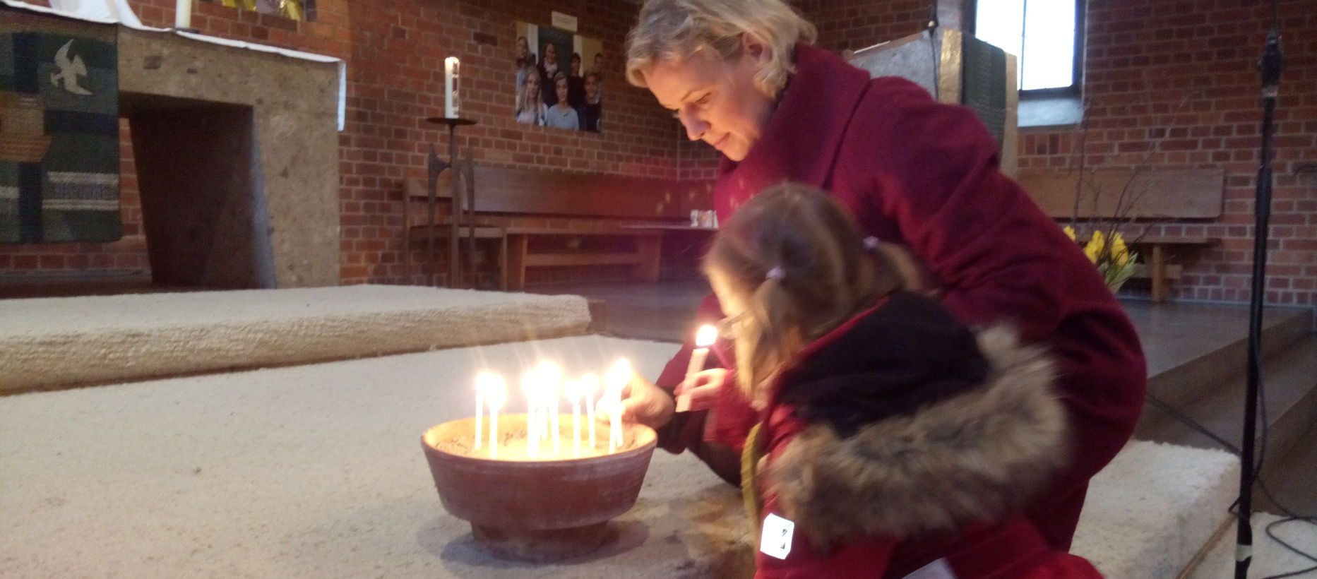 Äiti ja lapsi sytyttävät kynttilää kirkossa.